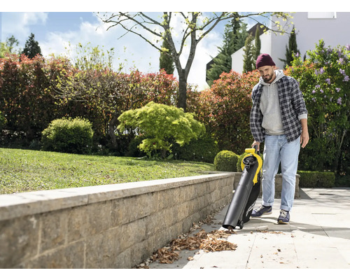 Un homme utilise un aspirateur de feuilles dans le jardin.