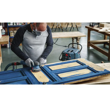 Artisan ponçant une porte bleue avec une ponceuse dans un atelier.
