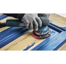 Une personne ponce un morceau de bois avec une ponceuse excentrique pour enlever les restes de peinture.