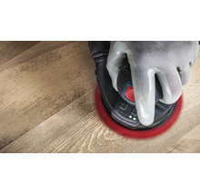 Une main gantée actionne une ponceuse excentrique sur une surface en bois.