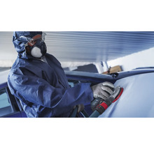 Personne en combinaison de protection ponçant une voiture avec une ponceuse.