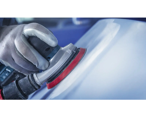 Hand mit Handschuh schleift eine Oberfläche mit einem Schleifgerät.