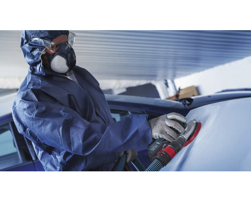 Eine Person mit Schutzanzug schleift ein Auto mit einem Schleifgerät.