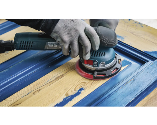 Eine Person schleift mit einem Exzenterschleifer ein blau gestrichenes Holzstück.