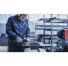 Ein Arbeiter schleift ein Metallgestell mit einem Schleifgerät in einer Werkstatt.