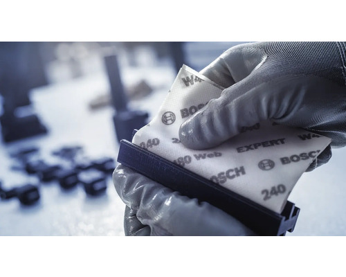 Eine Person mit Handschuhen befestigt Schleifpapier auf einem Handschleifer