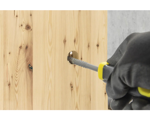 Eine Person verwendet eine Holzraspel, um ein Loch in ein Holzbrett zu erweitern.