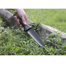 Une main tient un couteau de jardin pour désherber.