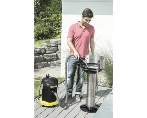 Un homme nettoie un gril à charbon de bois avec un aspirateur à cendres à l''extérieur.