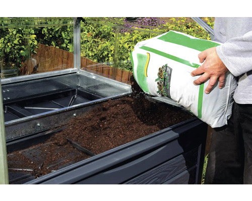 Un homme remplit de terre un potager surélevé dans une serre.