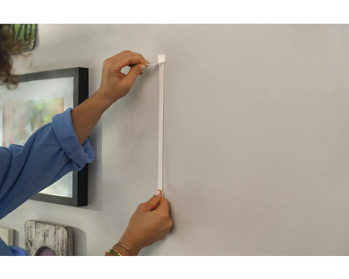 Person befestigt eine Bilderleiste an der Wand.