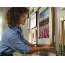 Frau hängt gerahmtes Bild an Wand