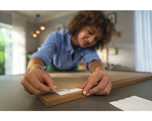 Frau befestigt Klebestreifen an einem Holzrahmen