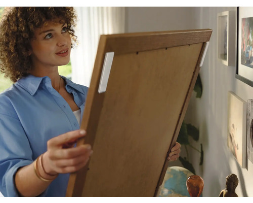 Frau befestigt Bild mit Klebestreifen an der Wand