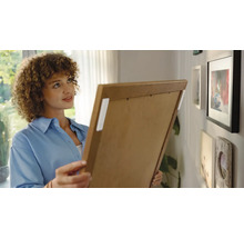 Frau befestigt Bilderrahmen mit Klebestreifen an der Wand