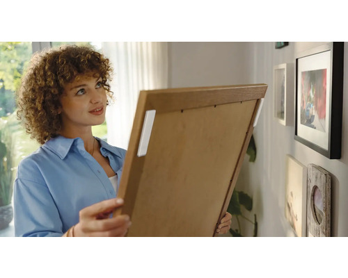 Frau befestigt Bilderrahmen mit Klebestreifen an der Wand