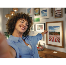 Frau zeigt auf gerahmtes Bild in einem hellen Wohnzimmer