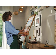 Frau hängt einen Bilderrahmen an einer Wand mit mehreren Rahmen auf.