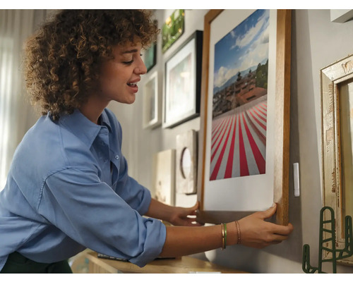 Frau hängt gerahmtes Bild an Wand