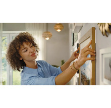 Frau richtet Bilderrahmen an der Wand aus. Dekoration für Wohnraumgestaltung.