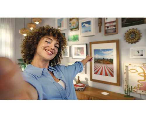 Frau zeigt auf eine Bildergalerie an der Wand in einem Wohnzimmer