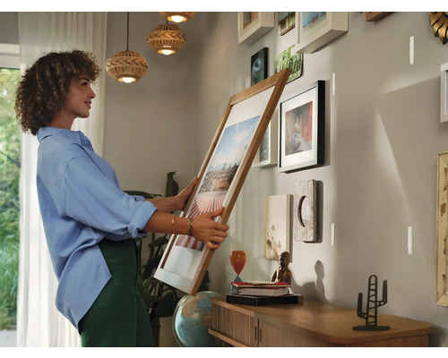 Frau hängt einen Bilderrahmen an eine Wand mit weiteren Bildern.