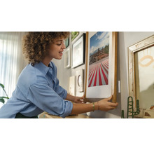 Frau hängt ein gerahmtes Bild an eine Wand