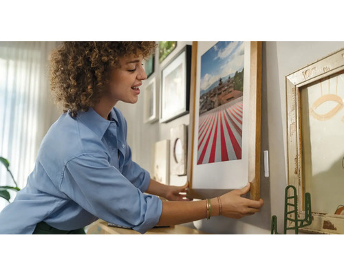 Frau hängt ein gerahmtes Bild an eine Wand