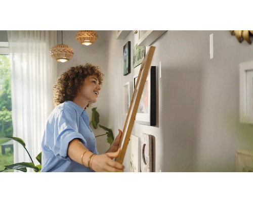 Frau hängt Bilderrahmen an einer Wand auf