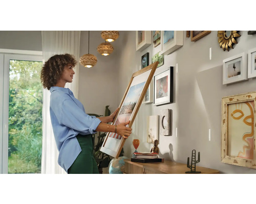 Frau hängt Bilderrahmen an Wand in hellem Raum