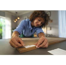 Frau befestigt einen Klebestreifen an einem Holzrahmen.