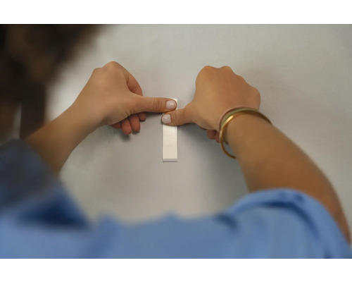 Eine Person befestigt einen Klebestreifen an einer Wand.