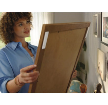 Frau befestigt ein Bild mit Klebestreifen an der Wand