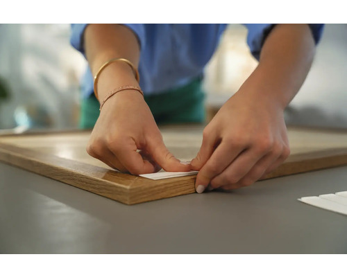 Eine Person befestigt eine Bildaufhängung an einem Holzrahmen.