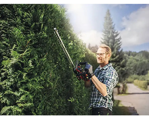 Un homme taille une haie avec un taille-haie dans le jardin.
