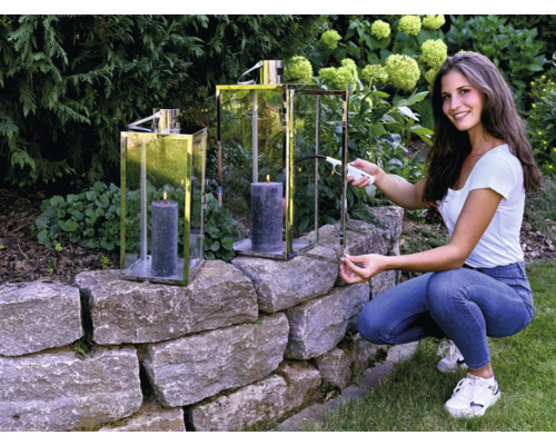 Frau zündet Kerze in Windlicht im Garten an