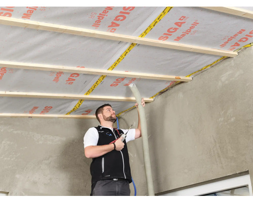 Un homme isole un toit avec un frein vapeur Siga Majpell et une sous-construction en bois.