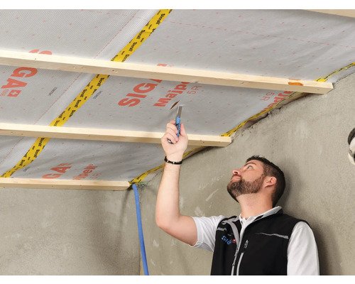 Un artisan fixe un frein-vapeur sur une structure en bois au plafond.