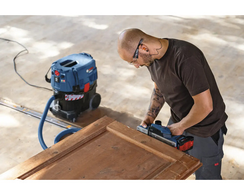 Artisan rabotant une porte en bois avec un rabot électrique et un aspirateur