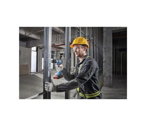 Un homme avec casque de sécurité et lunettes de protection utilise une visseuse sans fil dans une construction brute.