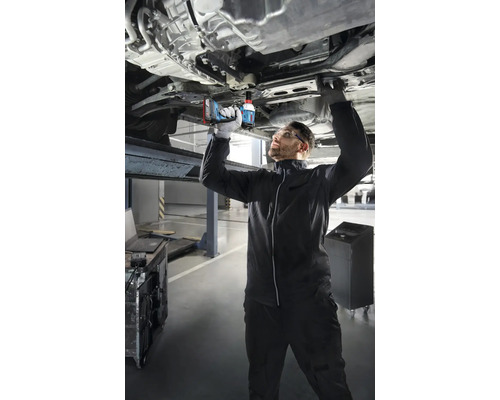 Un mécanicien travaille avec une clé à chocs sans fil sur une voiture sur un pont élévateur.