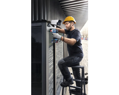 Un artisan monte une caméra de surveillance sur une échelle à l'aide d'une visseuse sans fil.