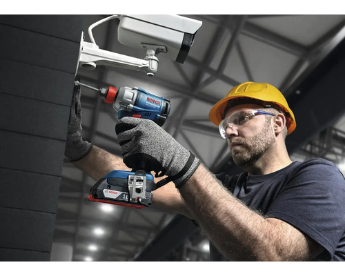 Un homme portant des lunettes de protection et un casque fixe une caméra de surveillance avec une visseuse à percussion sans fil Bosch.