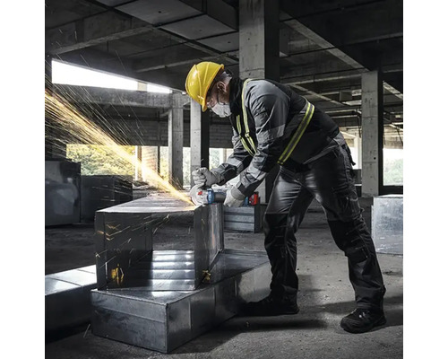 Ein Mann mit Schutzhelm schleift Metall mit einem Winkelschleifer, wobei Funken fliegen.