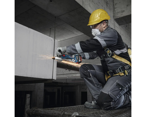 Handwerker mit Schutzhelm, Schutzbrille und Atemschutzmaske bei der Arbeit mit einem Akku-Winkelschleifer.