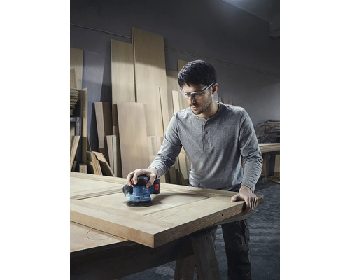 Un homme ponce une porte en bois avec une ponceuse excentrique dans l'atelier