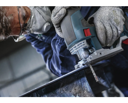 Un homme coupe du métal avec une scie sauteuse. Il porte des lunettes de sécurité, un masque respiratoire et des gants.