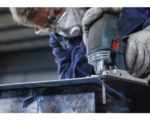 Une personne portant un masque respiratoire scie une pièce métallique avec une scie sauteuse.