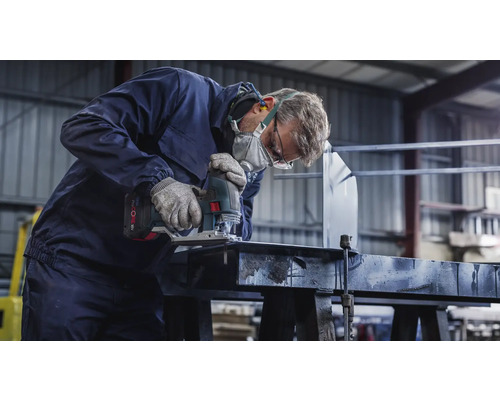 Un artisan portant un masque de protection et des lunettes de sécurité scie une pièce à travailler avec une scie sauteuse.