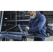 Un artisan coupe une pièce métallique avec une scie sauteuse. Il porte des vêtements de protection.